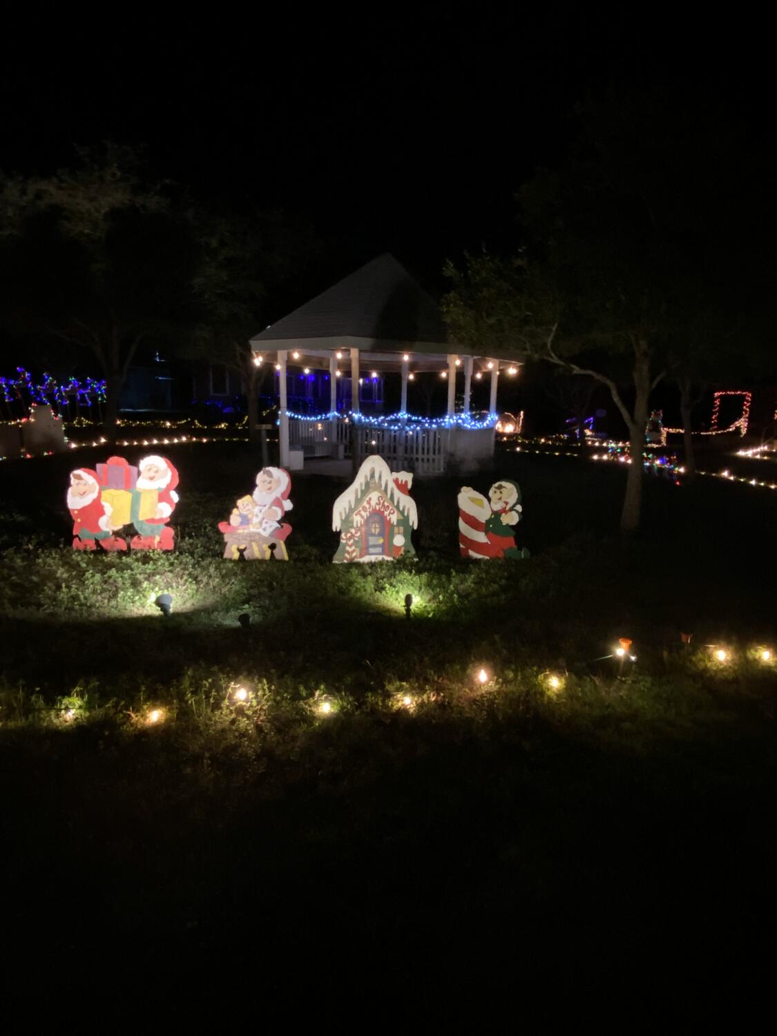 A lighted gazebo with painted Christmas cutouts on the lawn