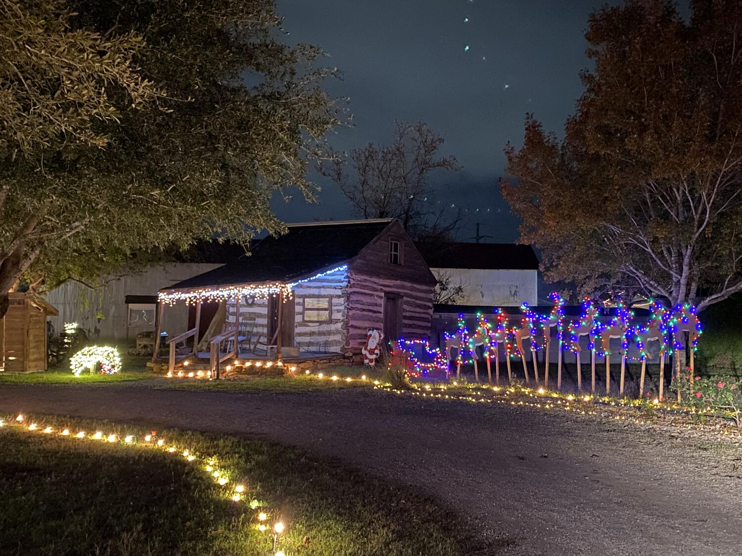 A log cabin in the Heritage Village trimmed in Christmas lights with lighted reindeer beside it